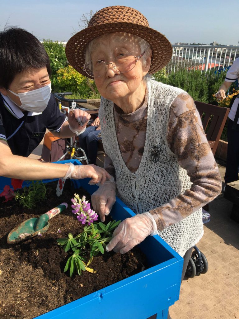 スタッフと一緒に花を植える女性