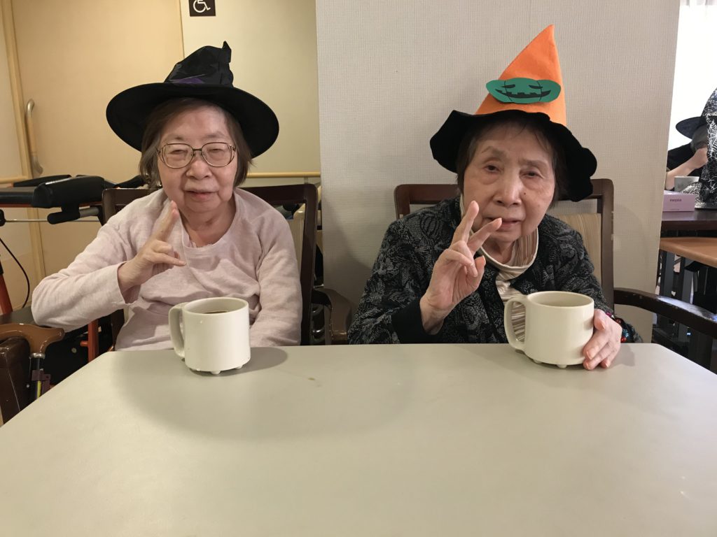 魔女の帽子をかぶってお茶を飲みながら楽しむ女性二人。