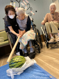 入居者とスタッフがスイカを前に笑顔で過ごす夏の季節行事風景