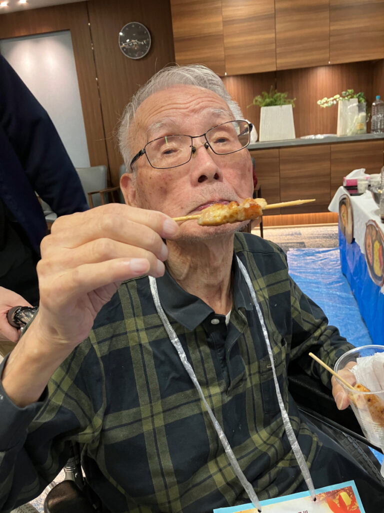 屋台グルメの焼き鳥を食べるご入居者