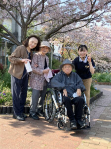 桜の下で入居者と職員が一緒に過ごす風景。春の季節行事の様子。